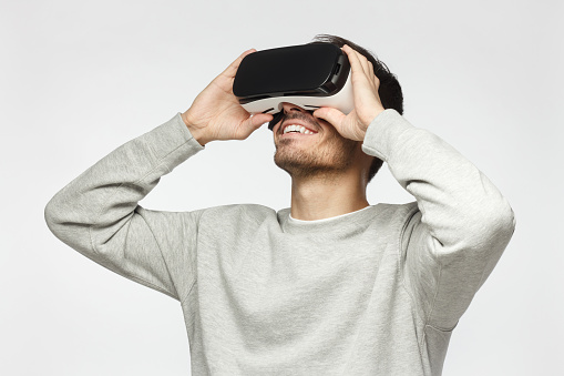 Handsome man playing video games in VR goggles or 3d glasses, wearing virtual reality headset for on his head