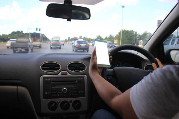 Female driver hands holding the car steering panel with holding blank smart phone on the highway
