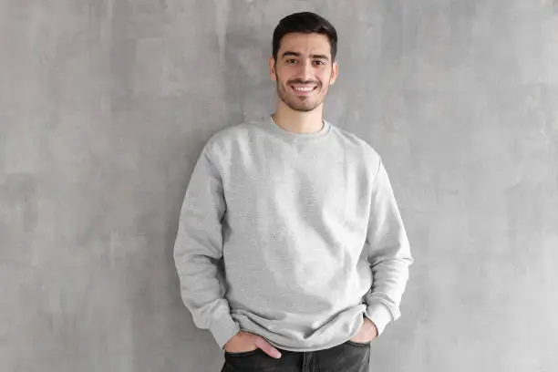 Photo of Young man in oversized sweatshirt isolated on textured gray wall background