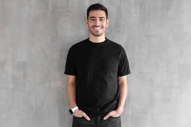 hotizontal porträt des jungen mannes tragen leeres schwarzes t-shirt und jeans, posieren gegen graue strukturierte wand - hotizontal stock-fotos und bilder