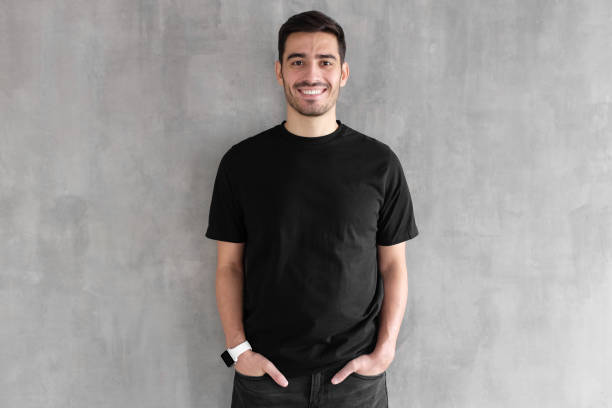 hotizontal portrait of young man wearing blank black t-shirt and jeans, posing against gray textured wall - hotizontal imagens e fotografias de stock