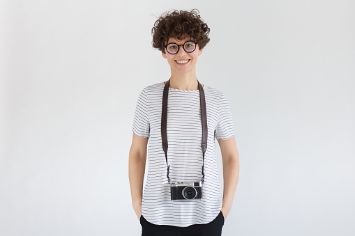 Smiling female photographer with retro film photo camera, standing isolated on gray background