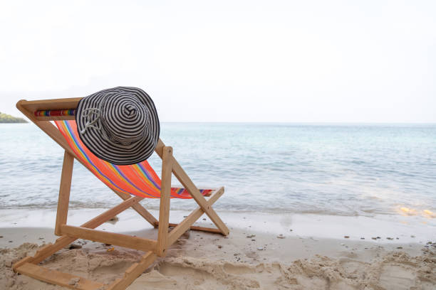 The orange beach chair and hat is on the clear sand beach with sea in background stock photo