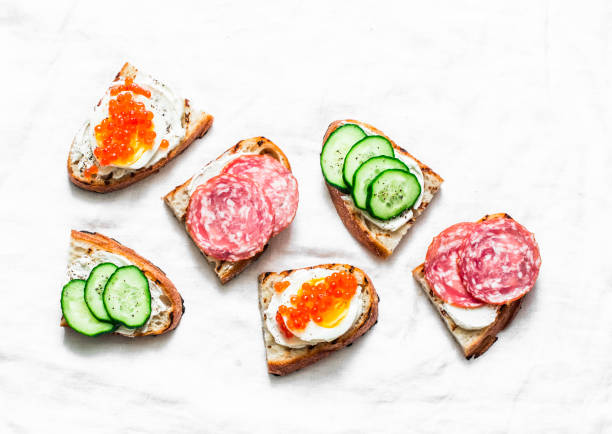 istock Appetizer sandwiches with red caviar, egg, sausage, cucumber and cream cheese on white background, top view 1090917782