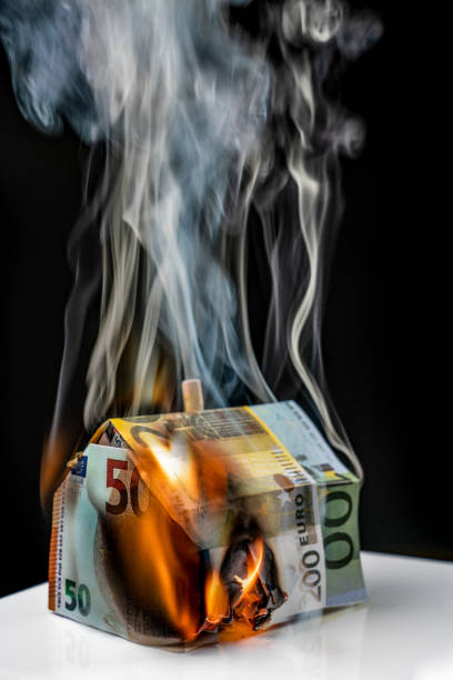 burning paper house made of euro banknotes against a black background stock photo