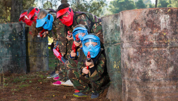 Kids paintball players aiming outdoors Group of boys and girls paintball players aiming and shooting with marker guns at opposing team outdoors paintballing stock pictures, royalty-free photos & images