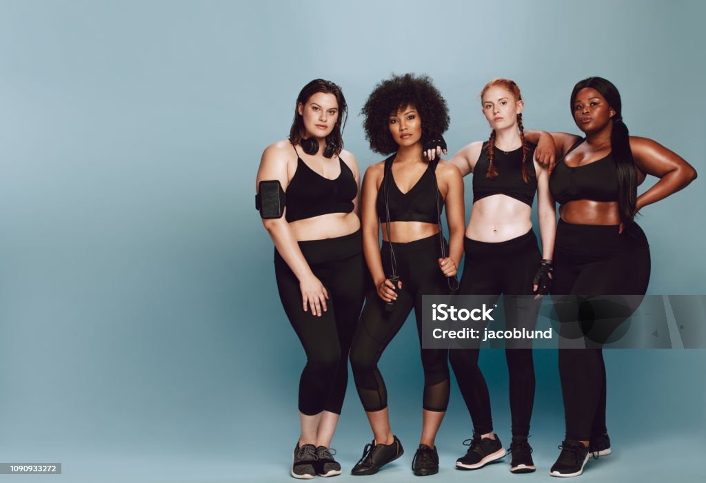Beautiful curvy women with good body Full length of multi-ethnic women with  in sportswear standing together over grey background. Three women of different race, figure type and size in fitness clothing. Women Stock Photo