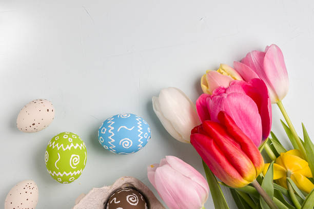 istock Painted easter eggs and bouquet of spring tulips closeup on a light blue background with space for congratulation 1090944198