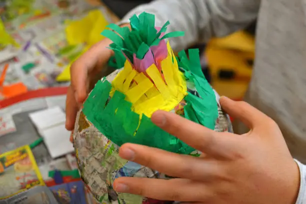 Children hands are making a pinata with colorful paper and glue.