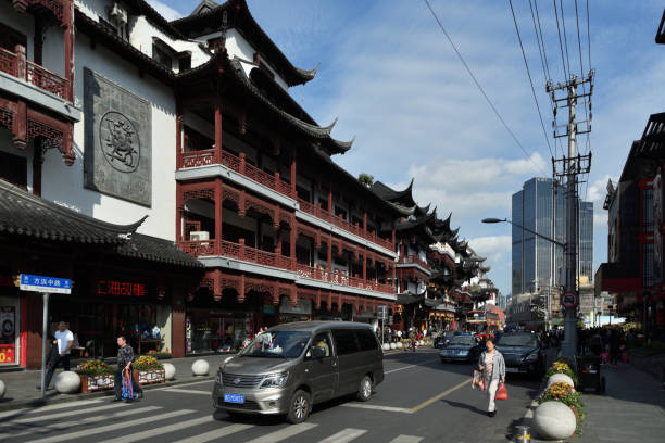An adult Chinese woman and two adult men in the street near the Yuyuan Gardens tourist attraction.  The traditional Chinese architecture with site offs and flying eaves provide a feeling of old China and the skyscraper in the background feels like new China.