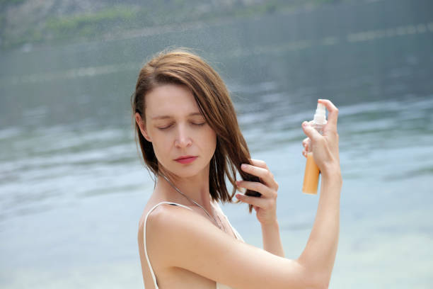 Woman applying sunscreen spray on the beach, hair care protection concept stock photo