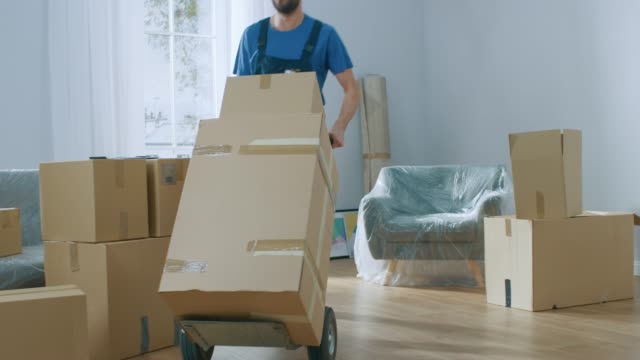 Professional Mover with Hand Truck Loads it With Cardboard Boxes and Helps People Move out and Relocate into the New House.