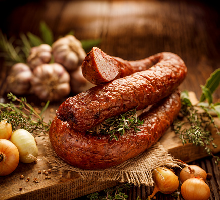 Smoked sausage on a wooden rustic table with addition of fresh aromatic herbs and spices, natural product from organic farm, produced by traditional methods