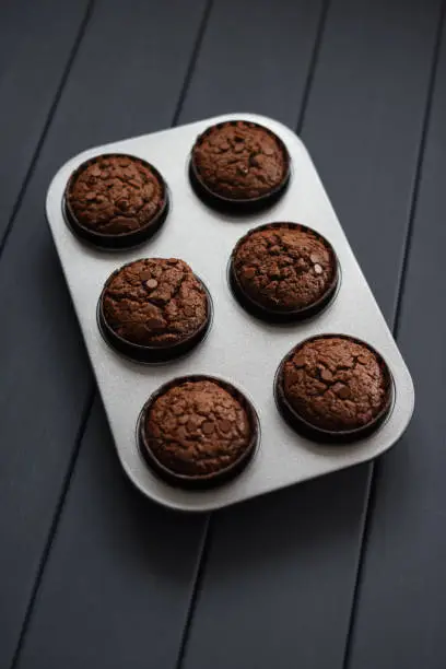 Homemade chocolate muffins in baking tray on dark background copyspace overhead view