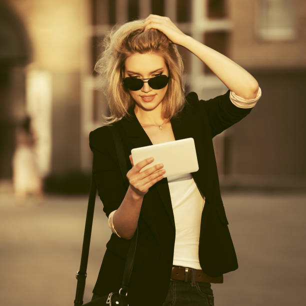Young fashion business woman in sunglasses using tablet computer on city street stock photo