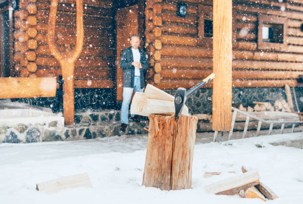mężczyzna przebywający we werrze w kraju. drewniany pniak z siekierą na ośnieżonym podwórku nieskoncentrowany ciężkimi płatkami śniegu. zimowe wakacje na wsi obraz koncepcji - wood cutting chopping fireplace zdjęcia i obrazy z banku zdjęć