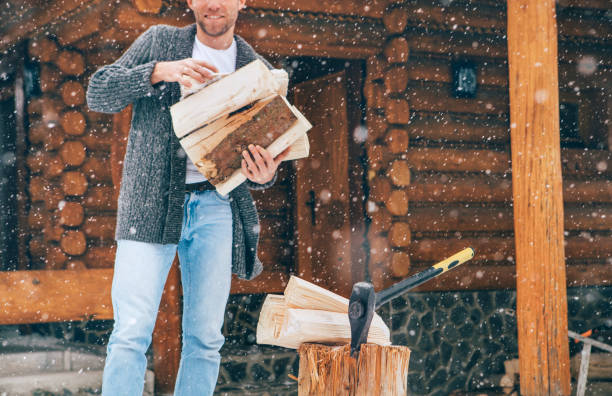 człowiek rąbanie drewna na ośnieżonym podwórku do kominka domu z ciężkimi płatkami śniegu tle . zimowe wakacje na wsi obraz koncepcji - wood cutting chopping fireplace zdjęcia i obrazy z banku zdjęć