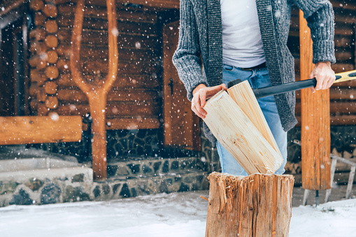 Man chopping wood on snowy yard for a house fireplace with heavy snowflakes background . Winter countryside holidays concept image