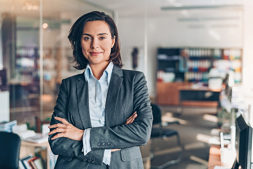 Confident and successful business woman in suit looking away and smiling. Portrait of mature black businesswoman standing in office with copy space. African american business woman in formal clothing standing in modern office: vision and future business company concept.