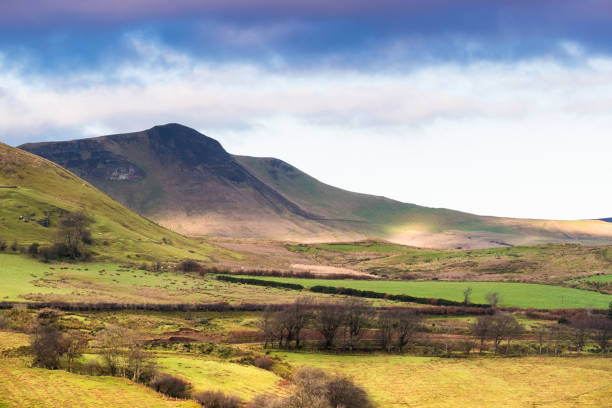 Dramatic purple-blue clouds over a sun-dappled landscape of green fields, hills, and mountains in Glenariff, County Antrim, Northern Ireland near Cushendall Mountain and fields in Glenariff, County Antrim, Northern Ireland glenariff photos stock pictures, royalty-free photos & images