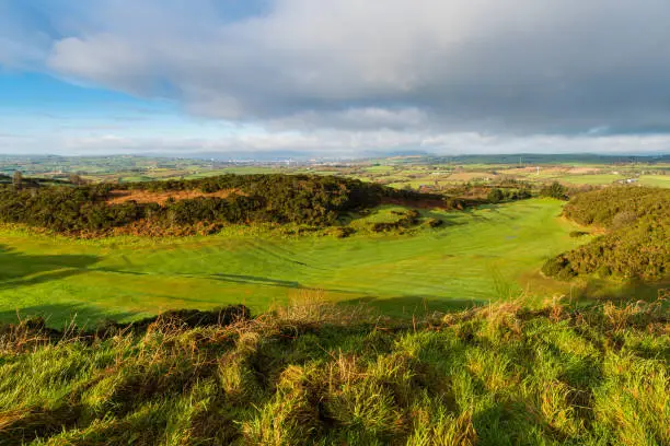 Photo of Eary morning golden hour light reveals a lush green golf course with a rolling landscape of grass and fields in the distance on the Ards Peninsula, County Down, Northern Ireland