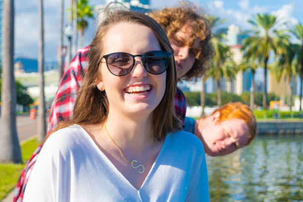 Young Woman Photobombed by Friends A smiling young woman is photobombed by her male friends photo bomb stock pictures, royalty-free photos & images