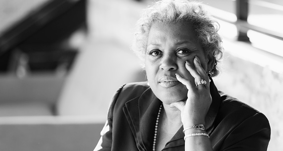 A mature African-American woman in her 50s sitting in an office, looking at the camera with a serious, perhaps confused, expression on her face.