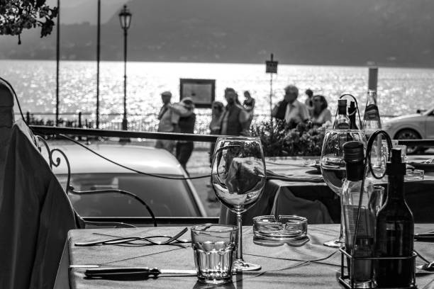 A table for two by the lakeside. Tourist pass by an empy table for two on the shore line of Varenna on Lake Como Italy. lake como photos stock pictures, royalty-free photos & images
