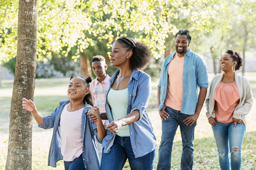 An African-American extended family taking a walk in the park together. The focus is on the 10 year old girl and her mother walking in front, holding hands.