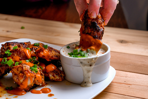 buffalo wing being dipped into ranch or bleu cheese dressing on a plate