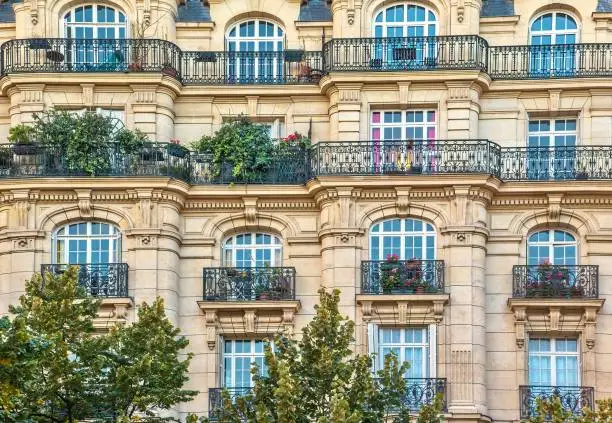 An ornate, stone apartment building facade in the 17th arrondissement of Paris, with beautiful arched windows and balconies with wrought iron railings and flower boxes.