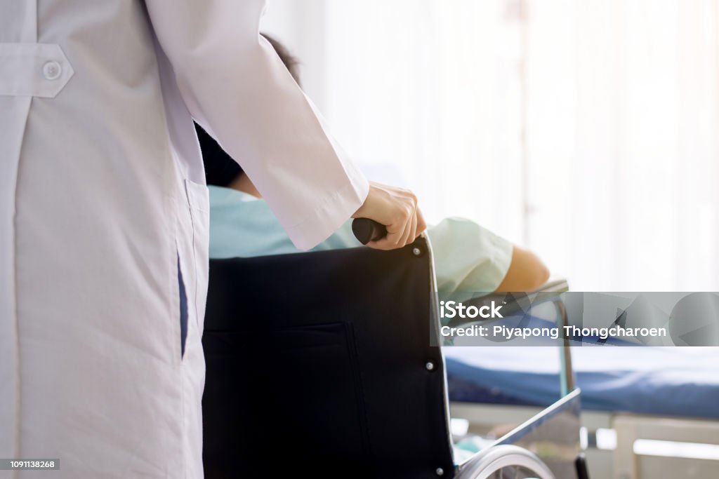 Patient woman is sitting in a wheelchair with doctor standing behind,Focus hand Leaving Stock Photo