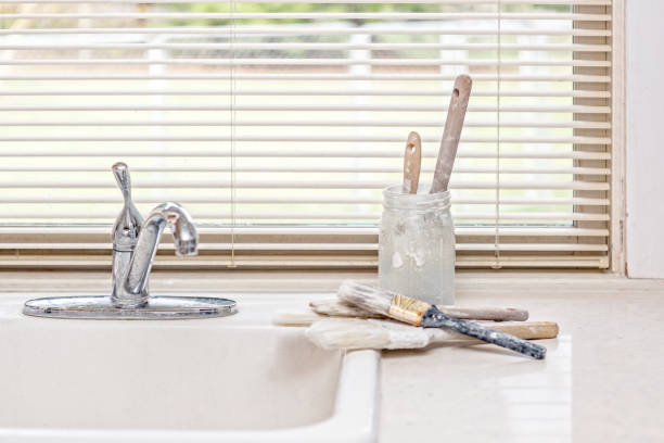 Freshly used paint brushes being cleaned, sitting on counter by utility sink.