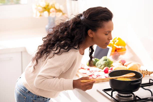 Chef woman enjoying the smell of freshly cooked soup. Cook woman enjoying the smell of freshly cooked soup, using a wooden spoon to taste the vegetarian soup. The woman with long black hair wearing a casual beige sweater and jeans. taste test stock pictures, royalty-free photos & images