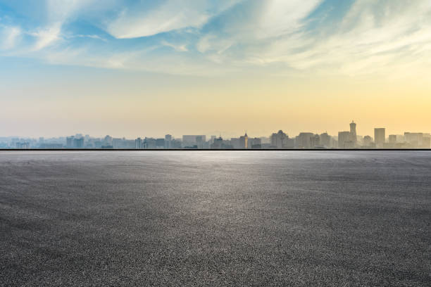 skyline der stadt und bauten mit leeren asphaltstraße bei sonnenaufgang - city street stock-fotos und bilder