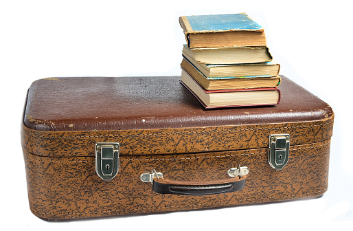 A stack of books on an old leather suitcase isolated on a white background.