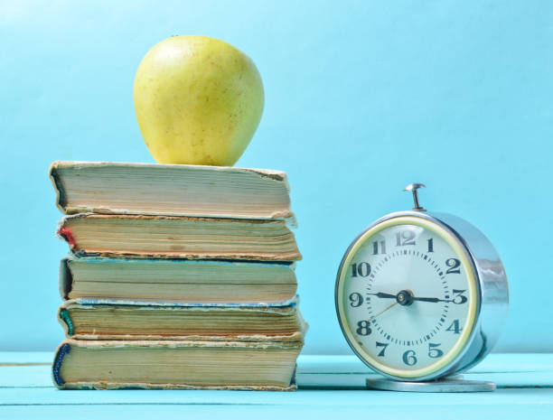 istock Alarm clock, stack old books, apple on a blue background. School concept, education 1091191340