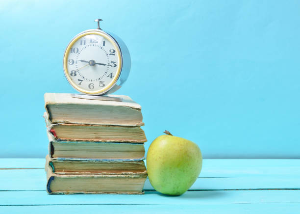 istock Alarm clock on stack of old books, apple on a blue background. School concept, education 1091191344