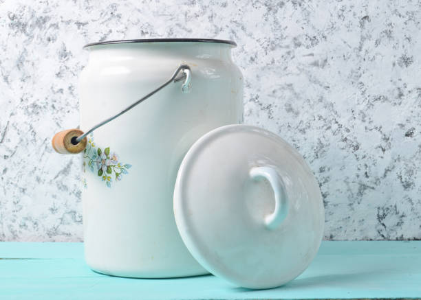 Enameled milk can with lid on white concrete wall background