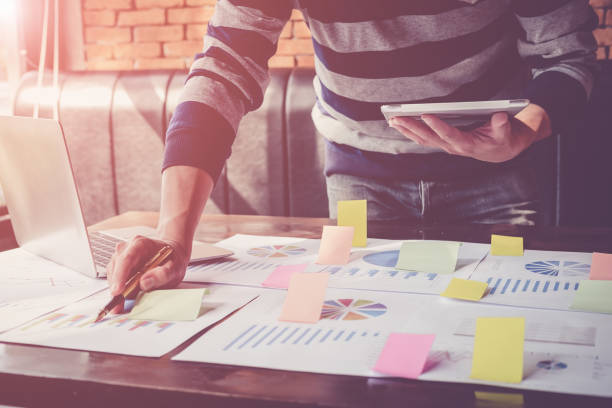 Asian business man hand holding note paper meeting working with new startup project use post it notes to share idea discussion and analysis data charts and graphs.Business finances and accounting concept