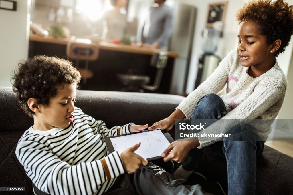 Fighting over touchpad at home! Small black siblings fighting over digital tablet in the living room. Fighting Stock Photo