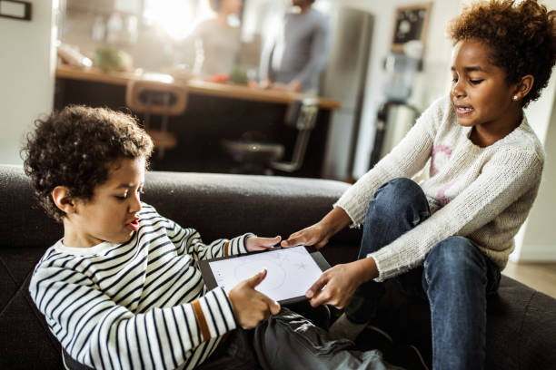 Fighting over touchpad at home! Small black siblings fighting over digital tablet in the living room. spar stock pictures, royalty-free photos & images