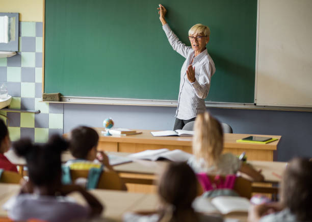 istock Senior female teacher writing a lecture on blackboard at elementary school. 1091229236