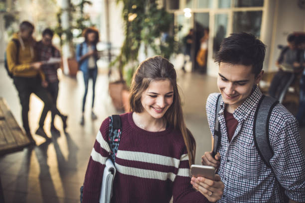 istock Happy high school friends reading a text message on smart phone in a hallway. 1091230926