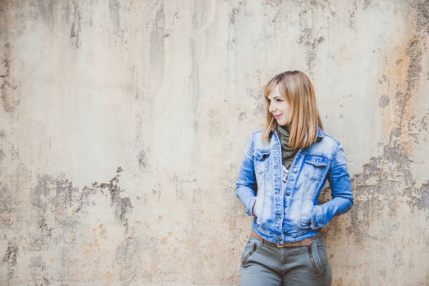 istock Young beautiful woman with denim jacket standing on a rusted wall 1091236678