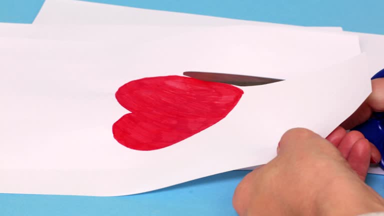 Woman cut out red heart shape on white paper