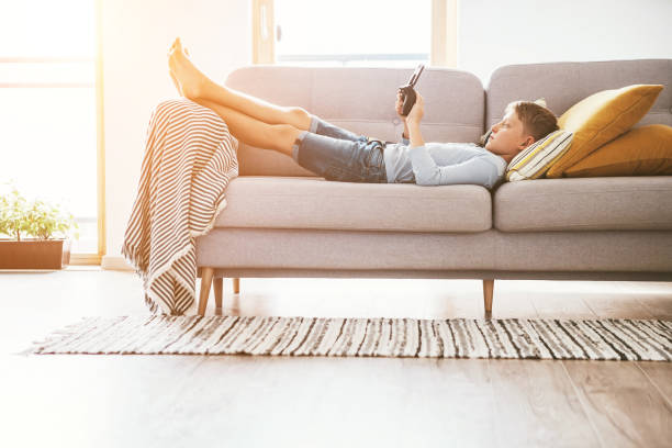 istock Boy plays with electronic devices - gamepad connected with smartphone lying on the cozy sofa in the home living room. 1091252224