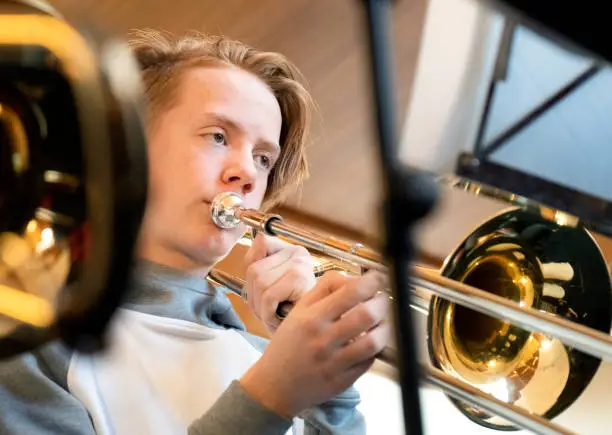 Young teenager musician playing the trombone. He is concentrating on reading his musical notes.