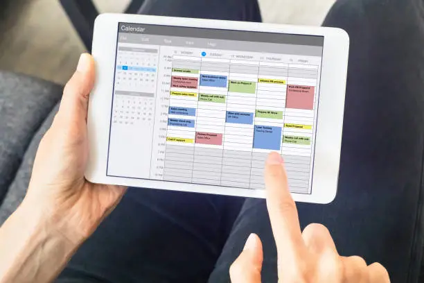 Photo of Calendar app on tablet computer with planning of the week with appointments, events, tasks, and meeting. Hands holding device, time management concept, organization of working hours planner, schedule
