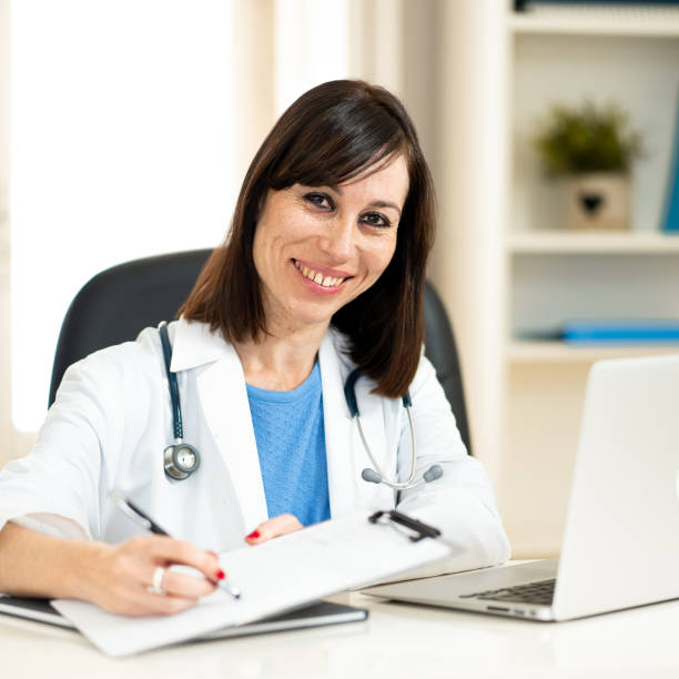 Portrait of happy attractive woman doctor working on paperwork, writting patient records and using laptop computer sitting on clinic hospital office desk in Health care and Medical insurance concept. retrato de médico mujer atractiva feliz trabajando en documentos, escribir registros de pacientes y uso de ordenador portátil sentado en escritorio de oficina de hospital de clínica en la atención de la salud y el concepto de seguro médico.